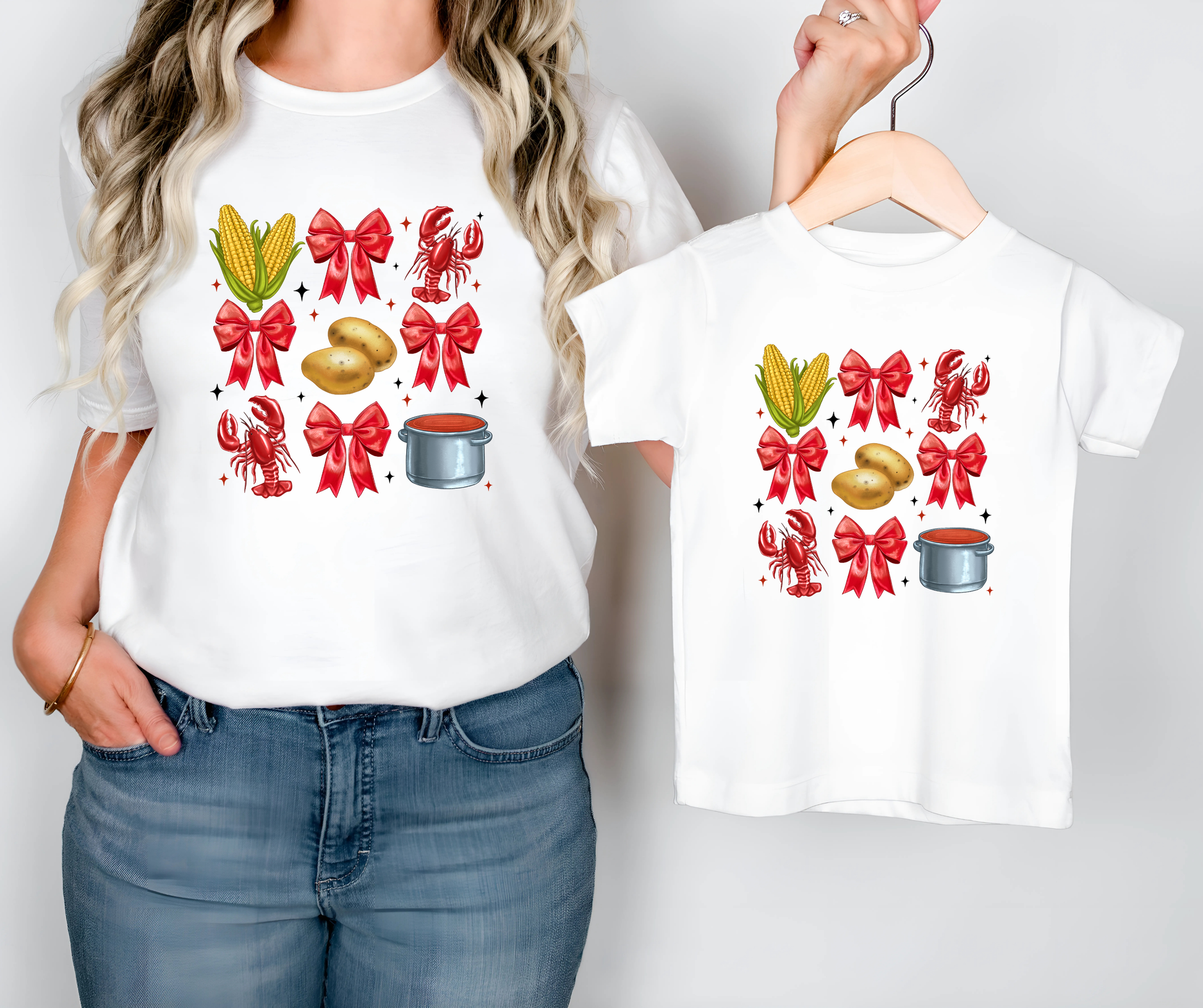 Person holding a white t-shirt with festive designs, including corn, bows, and pots, on a plain background.
